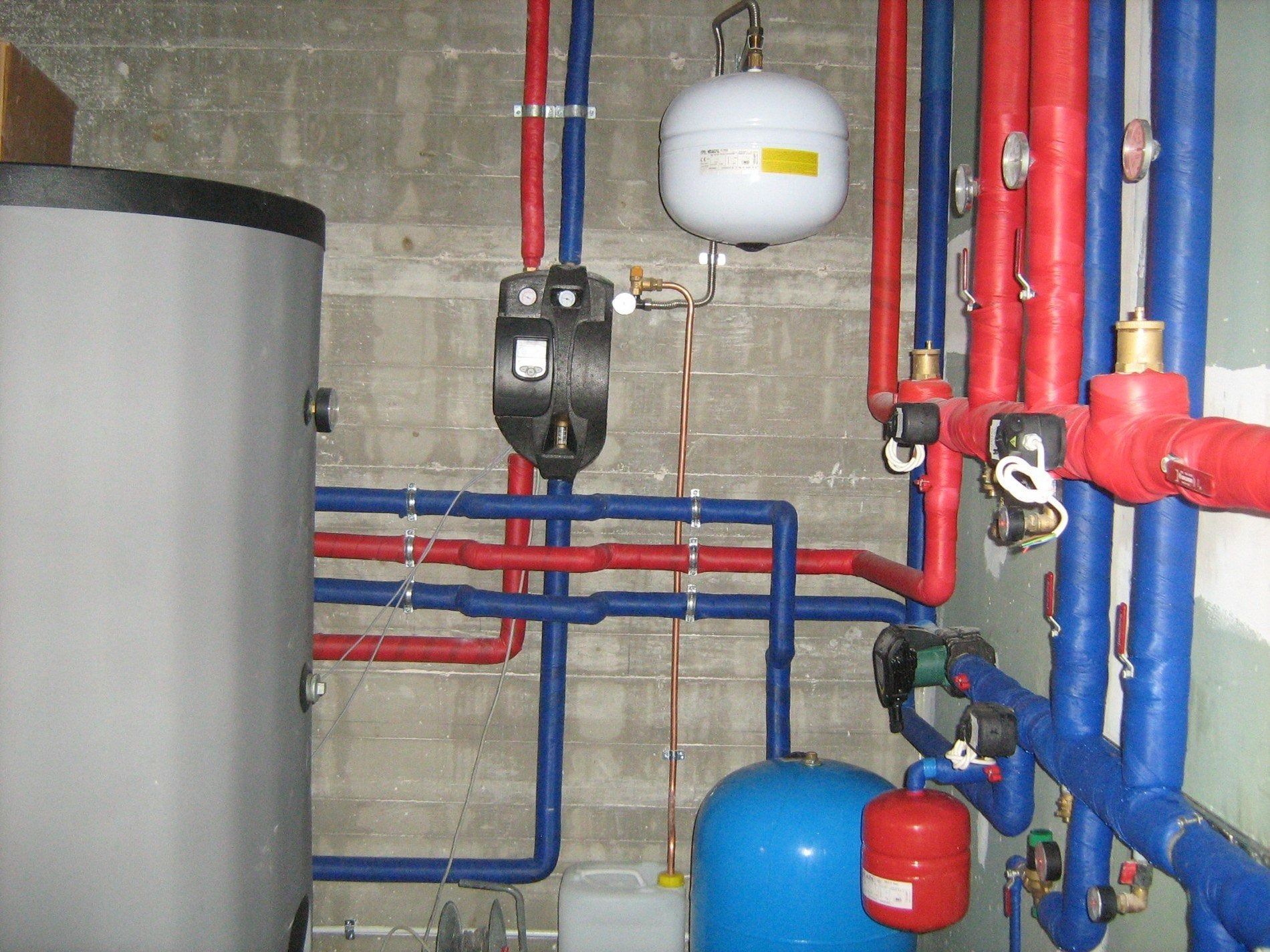 Una parete del seminterrato che mostra un impianto di riscaldamento con serbatoi per le acque grigie, tubi isolati blu e rossi e vasi di espansione.