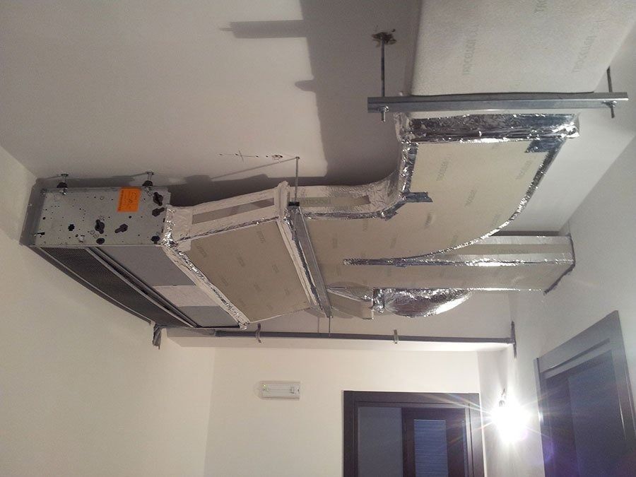 Unità interna di climatizzazione a soffitto con condotti metallici rivestiti con isolamento in alluminio, installata in una stanza non rifinita.
