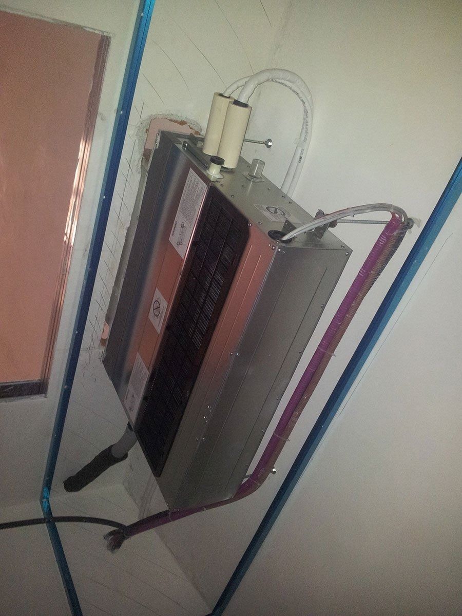 Uno scaldabagno elettrico montato su una parete bianca con tubi e cablaggi collegati.