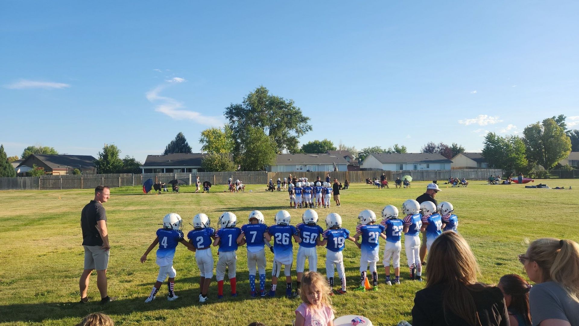 A group of young football players are standing in a field holding hands.