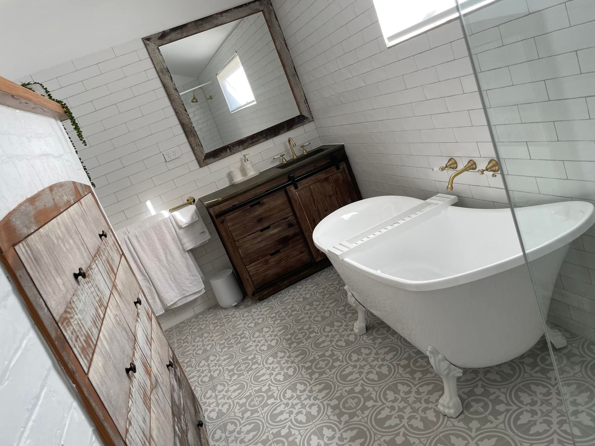 A bathroom with a tub , sink , mirror and dresser.