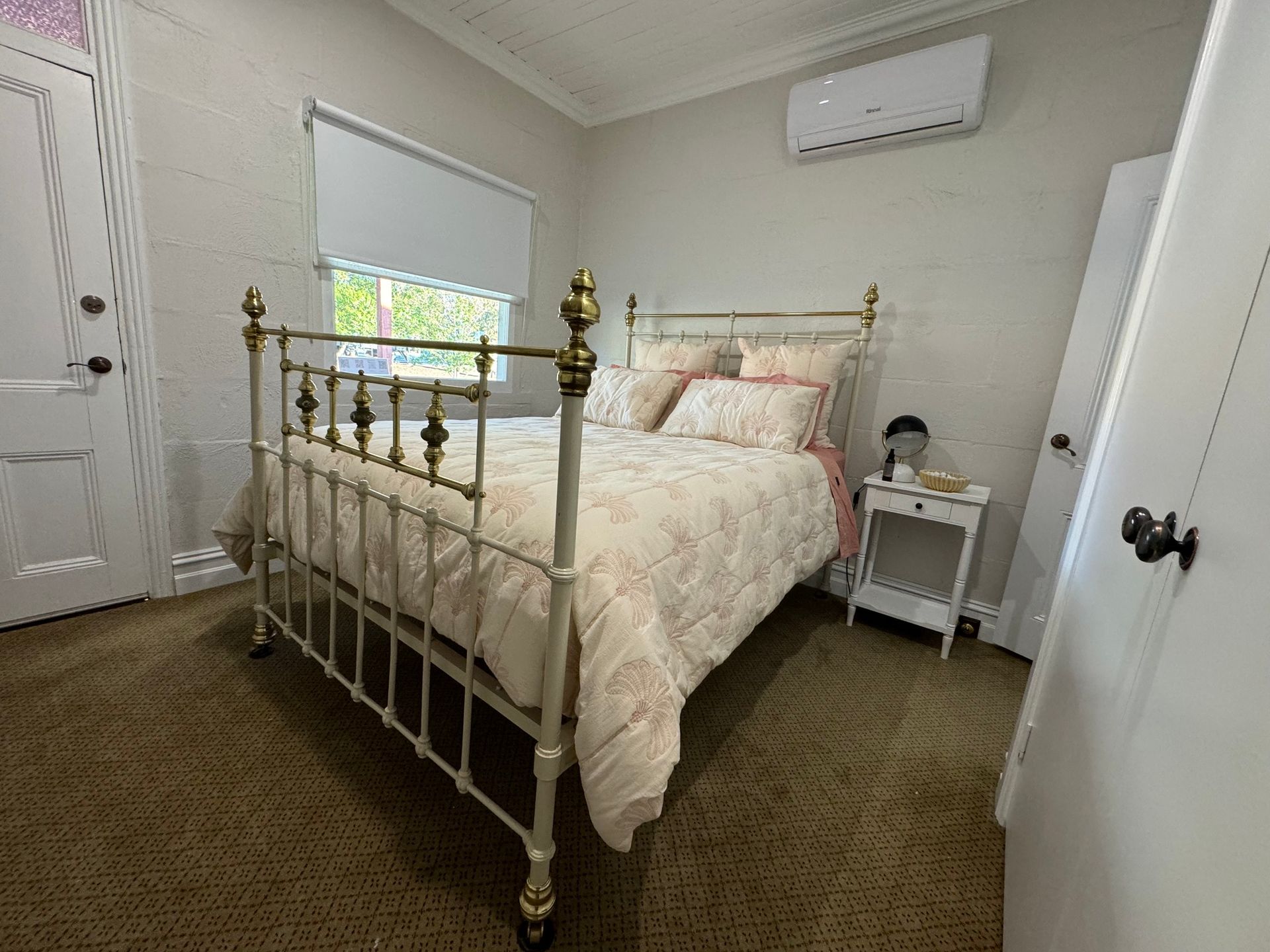Bedroom with a white bed, floral bedding, and small nightstand. Beige carpet and white walls.