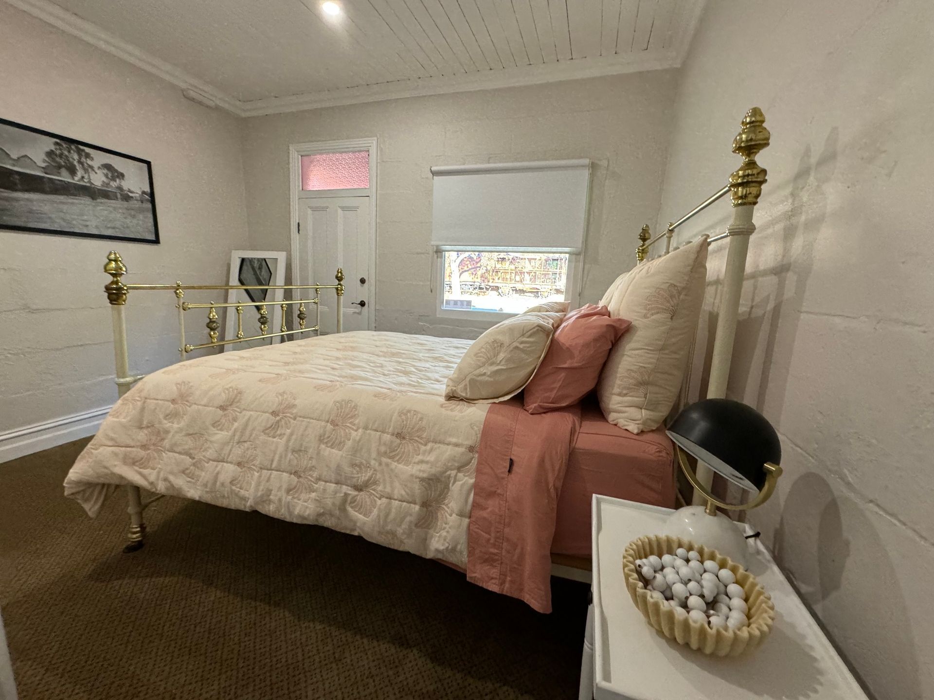 A bedroom with a bed , nightstand , lamp and window.
