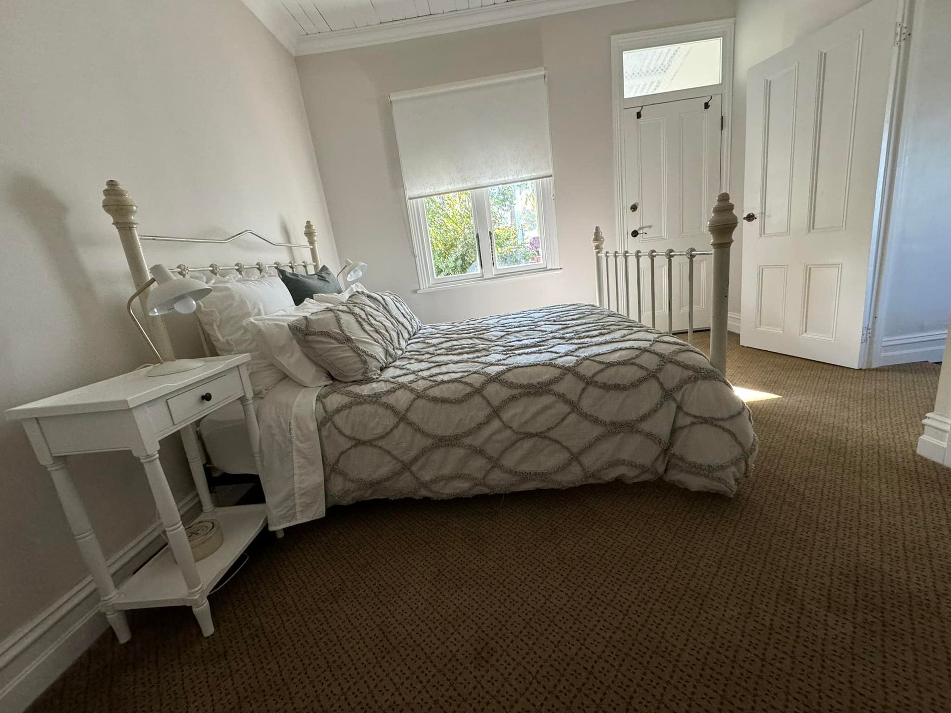 Bedroom with a white bed, nightstand, and a patterned comforter. Doorway on the right.