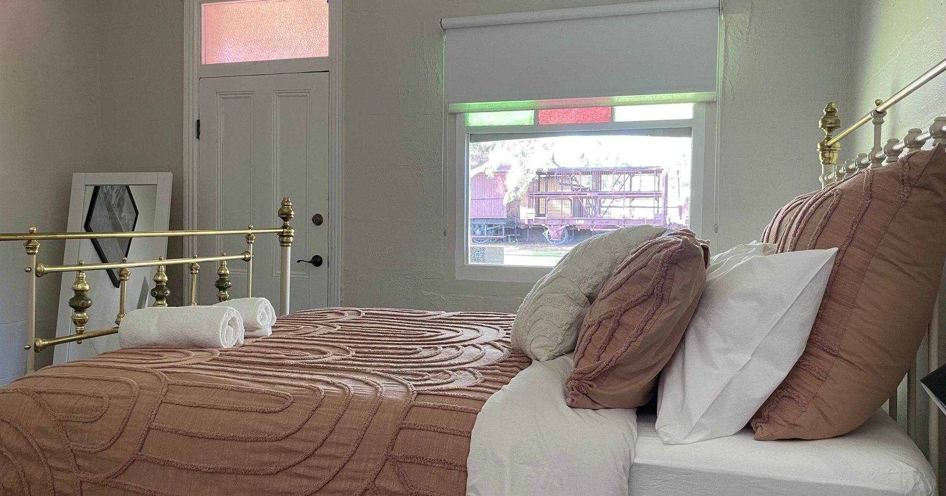 Bedroom with a brass bed, patterned bedding, and a window with stained glass.