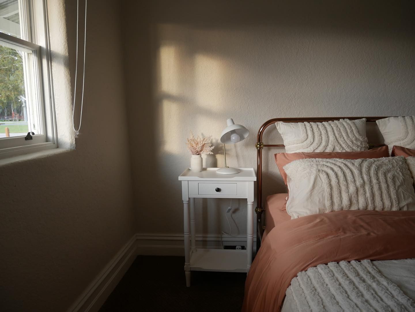 A bedroom with a bed , nightstand , lamp and window.