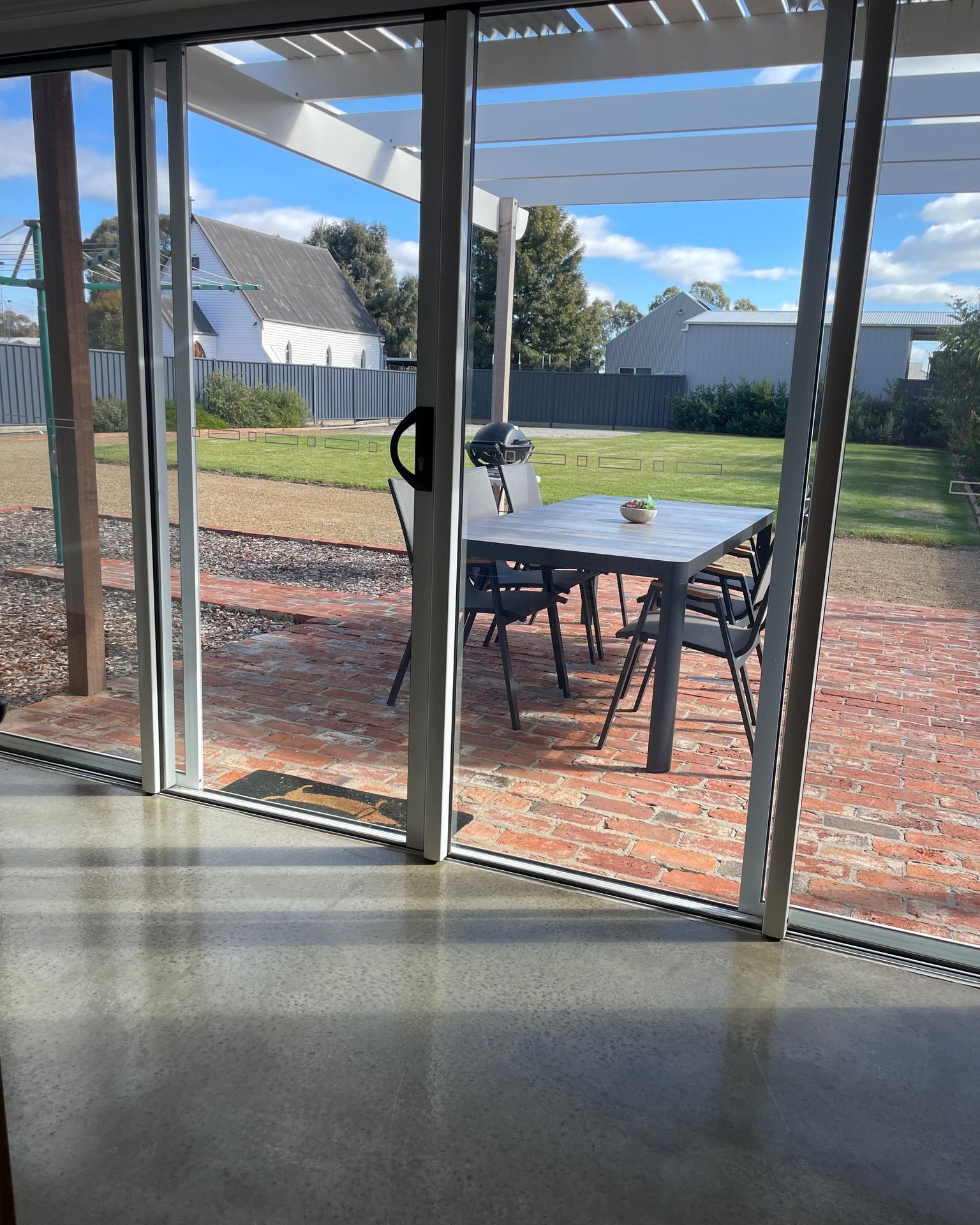 Sliding glass door open to a patio with table and chairs, a lawn, and a white house in the background.