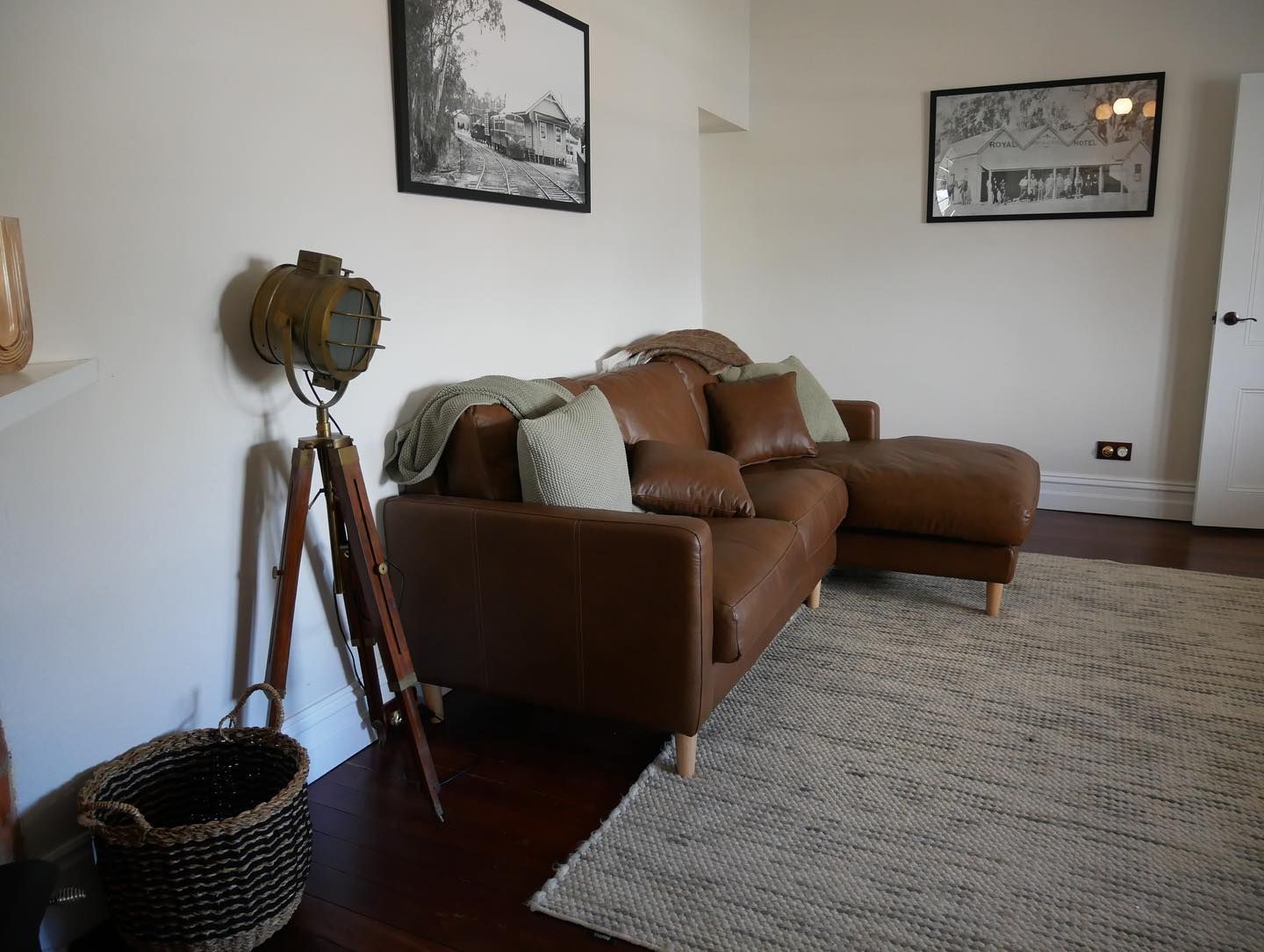 Brown leather sectional sofa in a white-walled living room with a rug, art, and a tripod floor lamp.