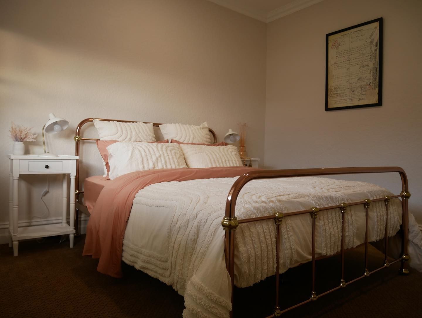 A bedroom with a bed , nightstand , lamps and a picture on the wall.