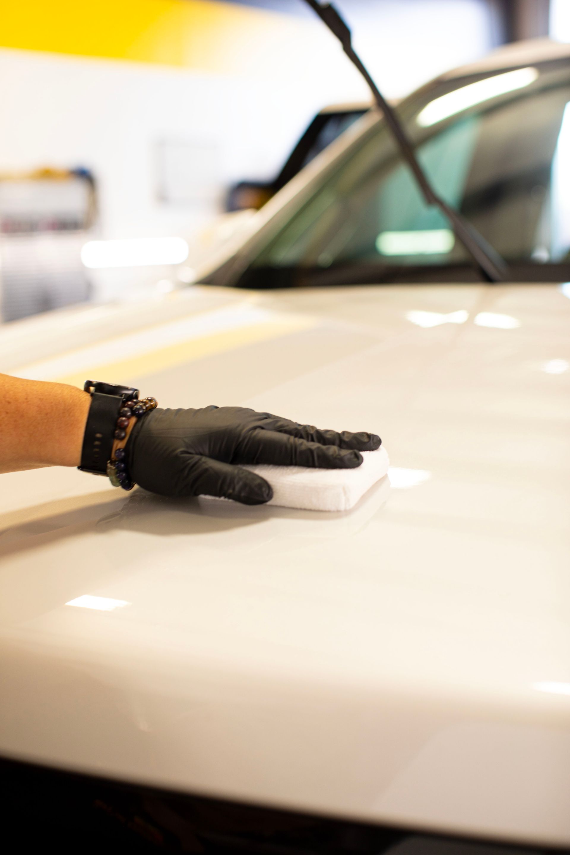 A person is wiping the hood of a white car with a ceramic coating applicator pad.