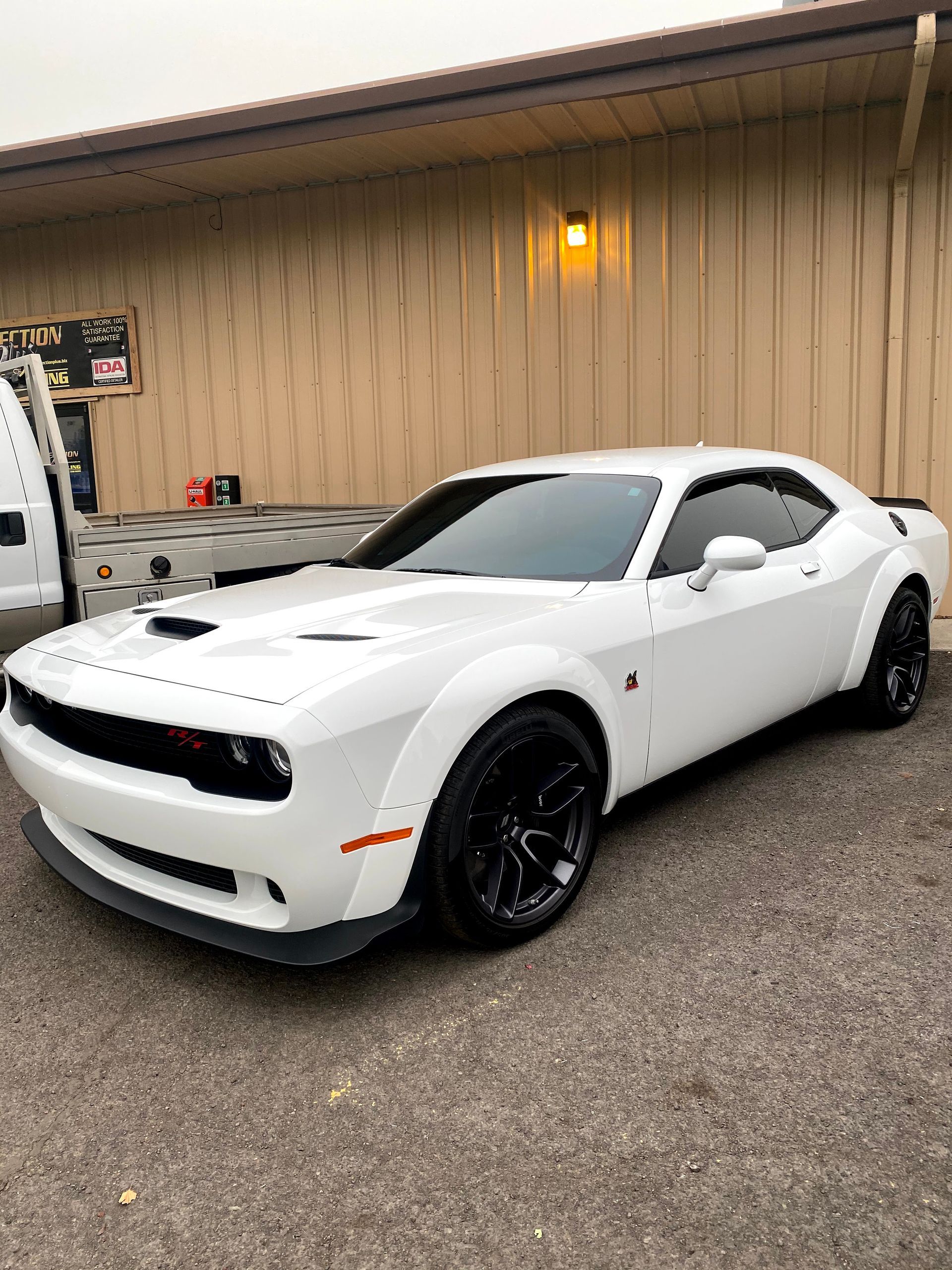 A white dodge challenger is parked in front of a building.