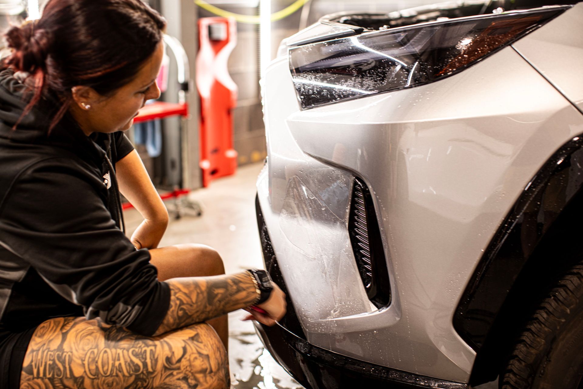 A woman is applying a protective film to the front of a car.