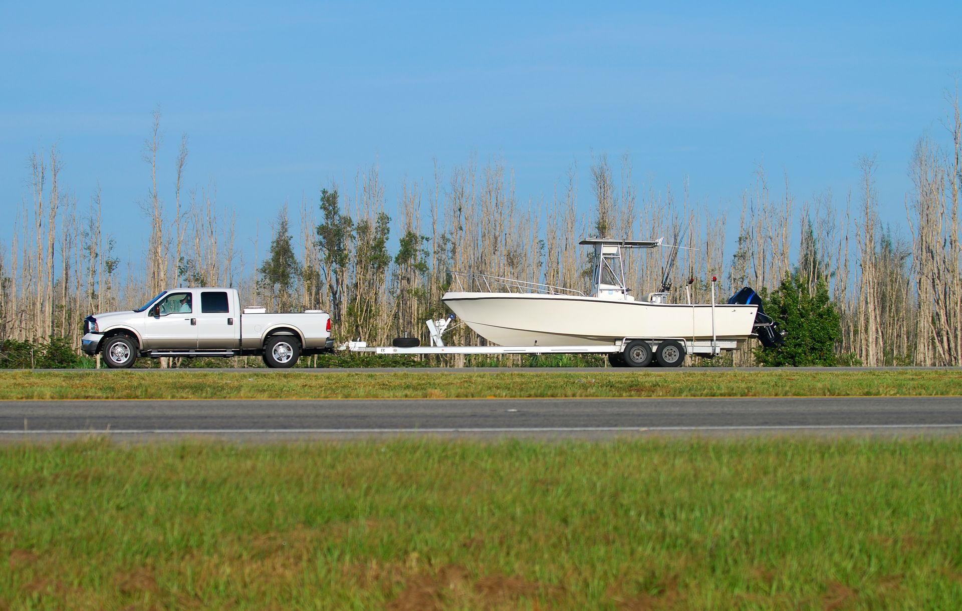 A white truck is towing a boat down a highway.