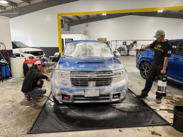Two men are washing a blue car in a garage.