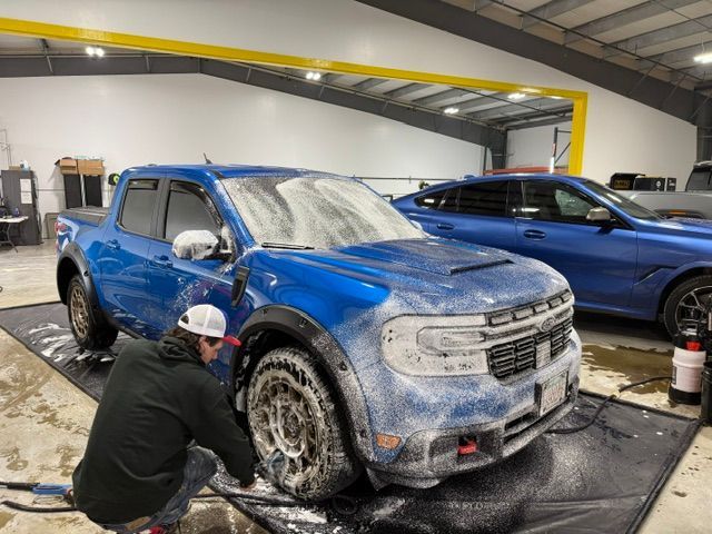 A man is washing a blue truck in a garage.