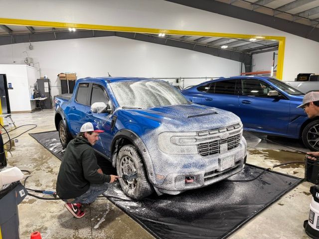 Two men are washing a blue truck in a garage.