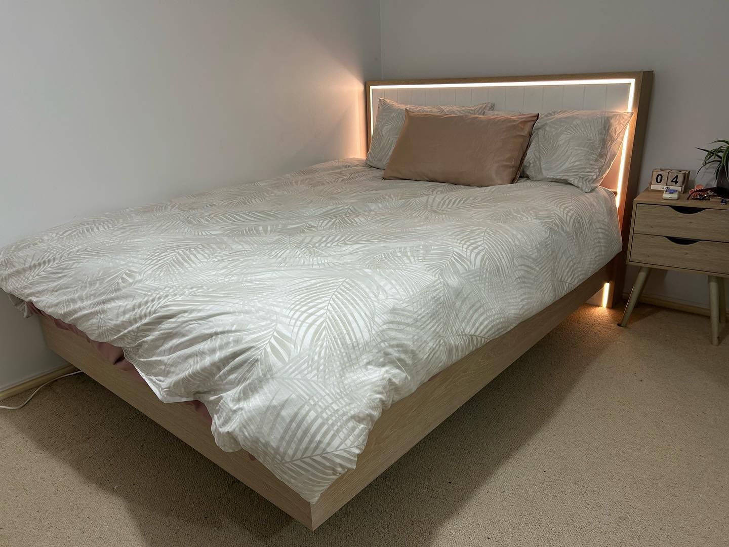 A Bed With a White Comforter and Pillows in a Bedroom With a Nightstand — Precision Kitchens & Cabinets in Ballina, NSW