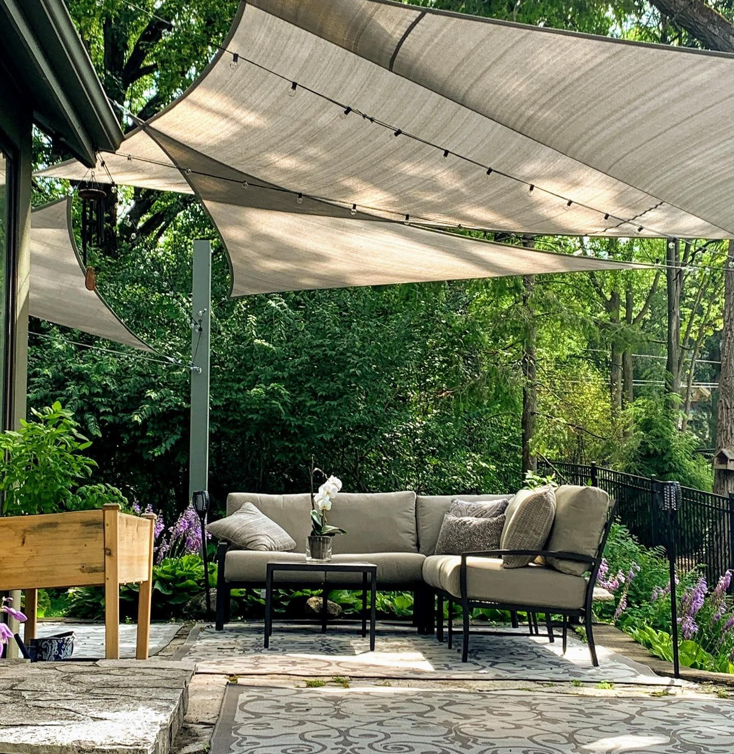 Patio with outdoor seating, a shade sail, and surrounding greenery.