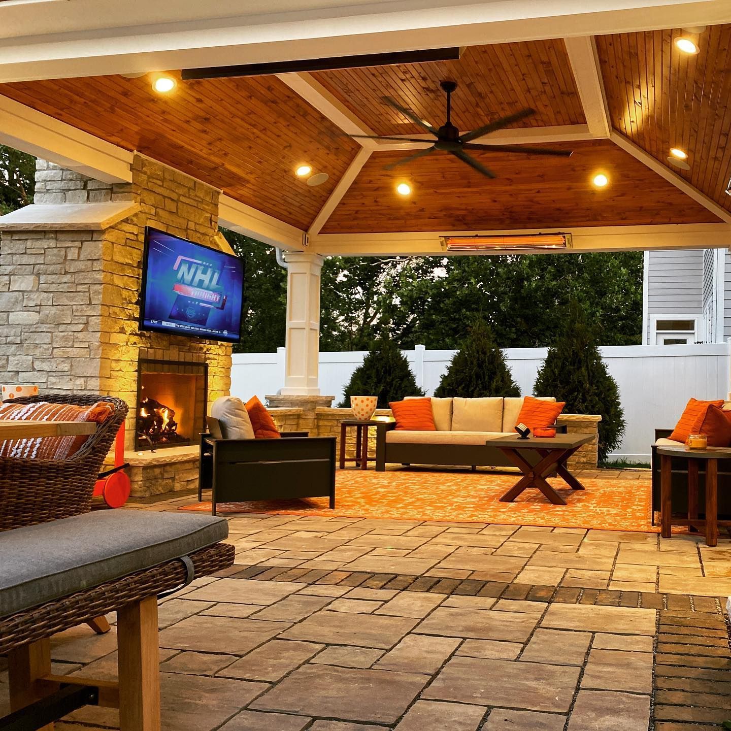 Patio with fireplace, TV, seating, and wooden ceiling, illuminated by lights.