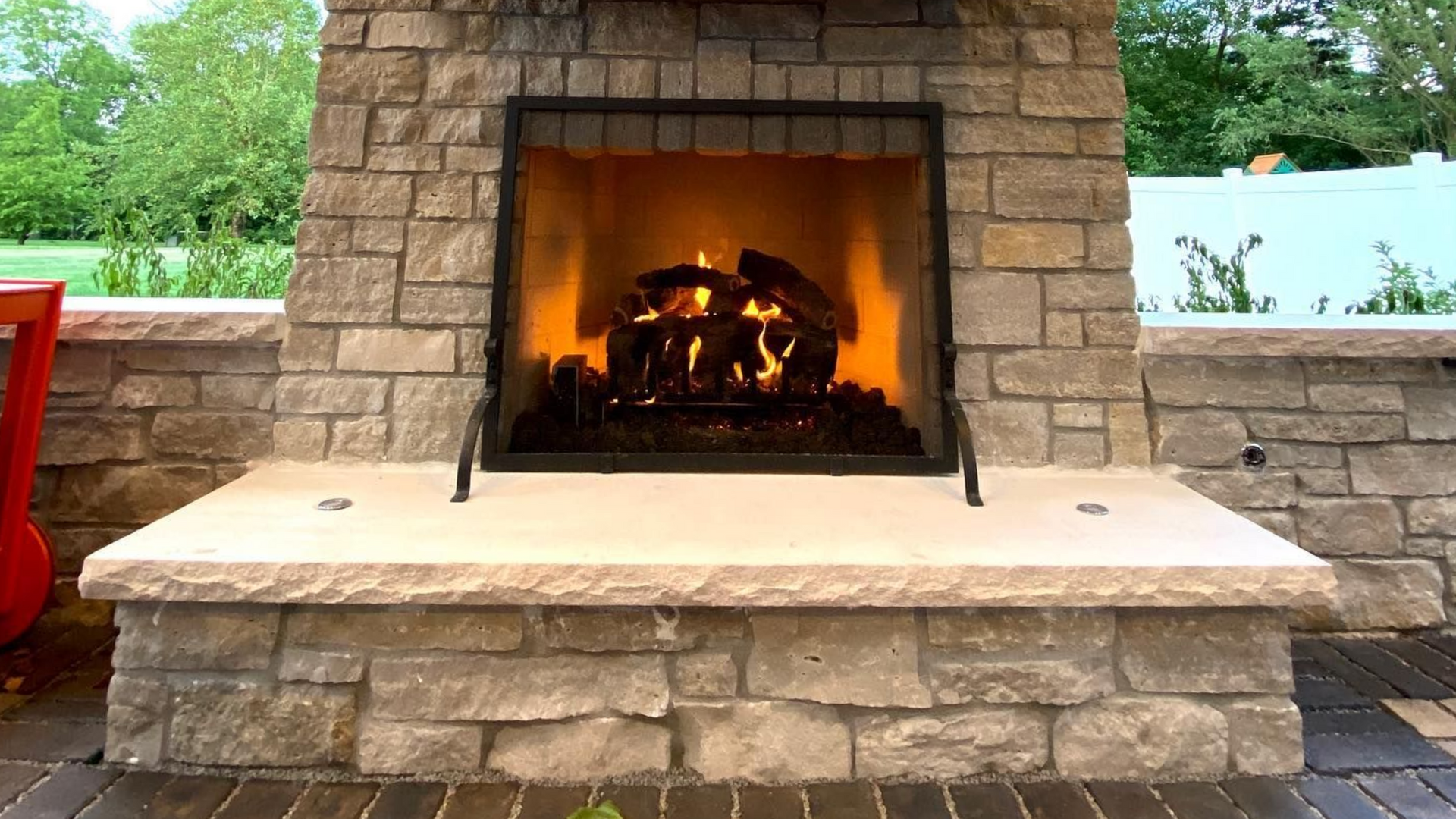 Stone outdoor fireplace with a burning fire, set on a patio.
