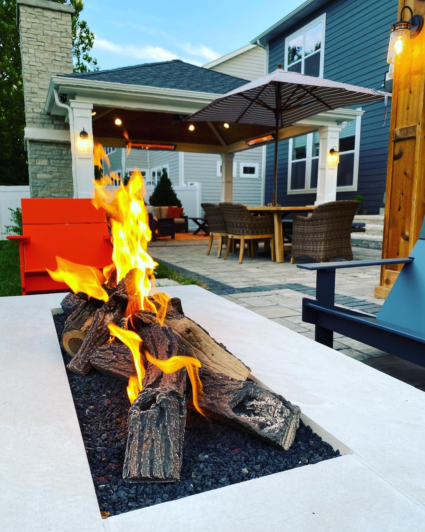 Outdoor fire pit with burning logs, patio with dining set, and a shaded pergola.