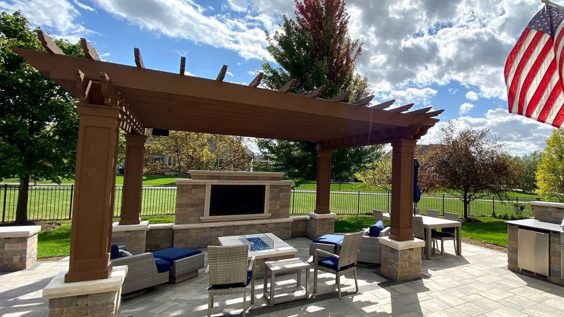 Outdoor patio with pergola, fireplace, and seating area. American flag waves in the background.