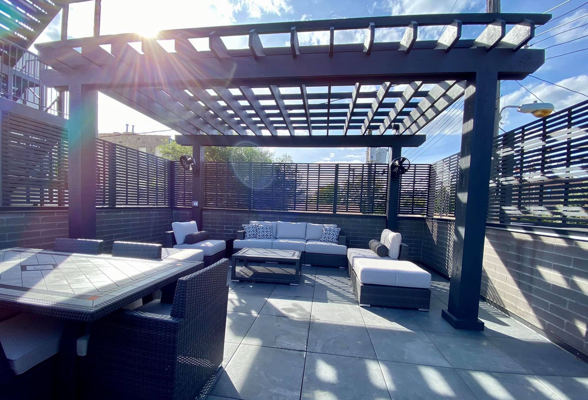 Outdoor patio with dark pergola, gray furniture, and dining set under a sunny sky.