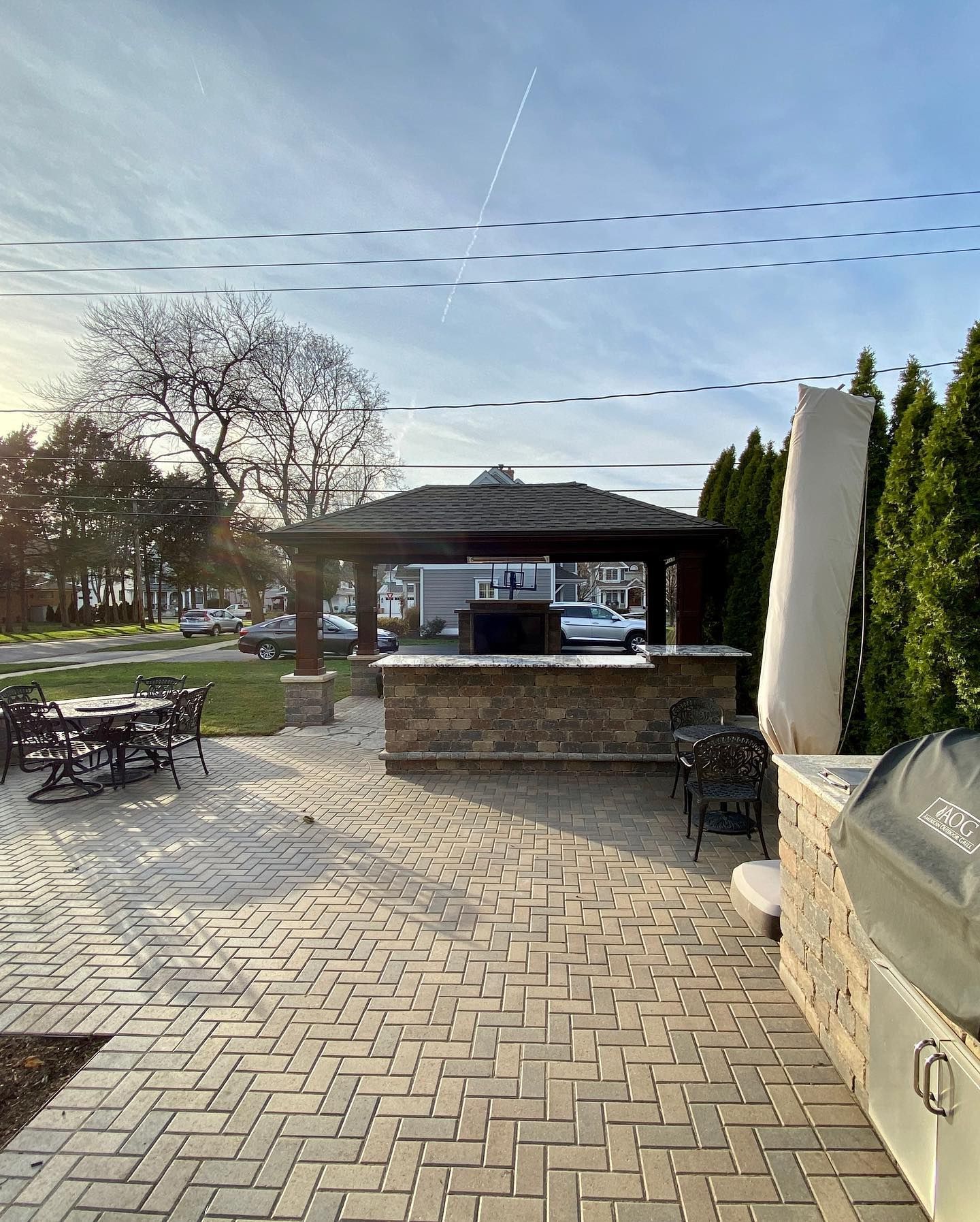 Outdoor kitchen with a brick patio and a gazebo. Grill and seating area visible.