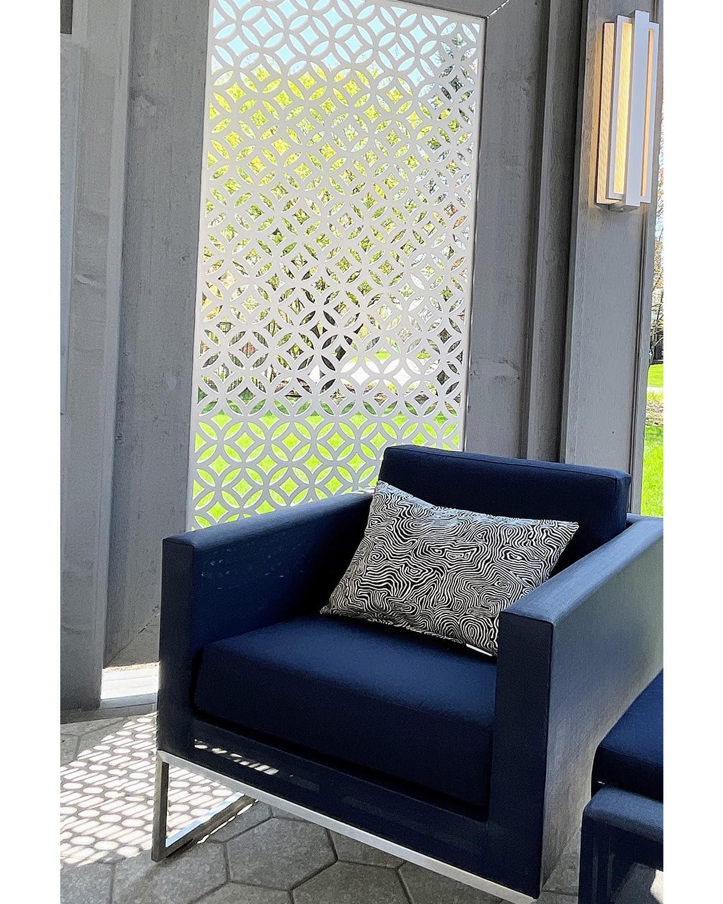 Navy armchair with patterned pillow, on patio, in front of a decorative white screen.