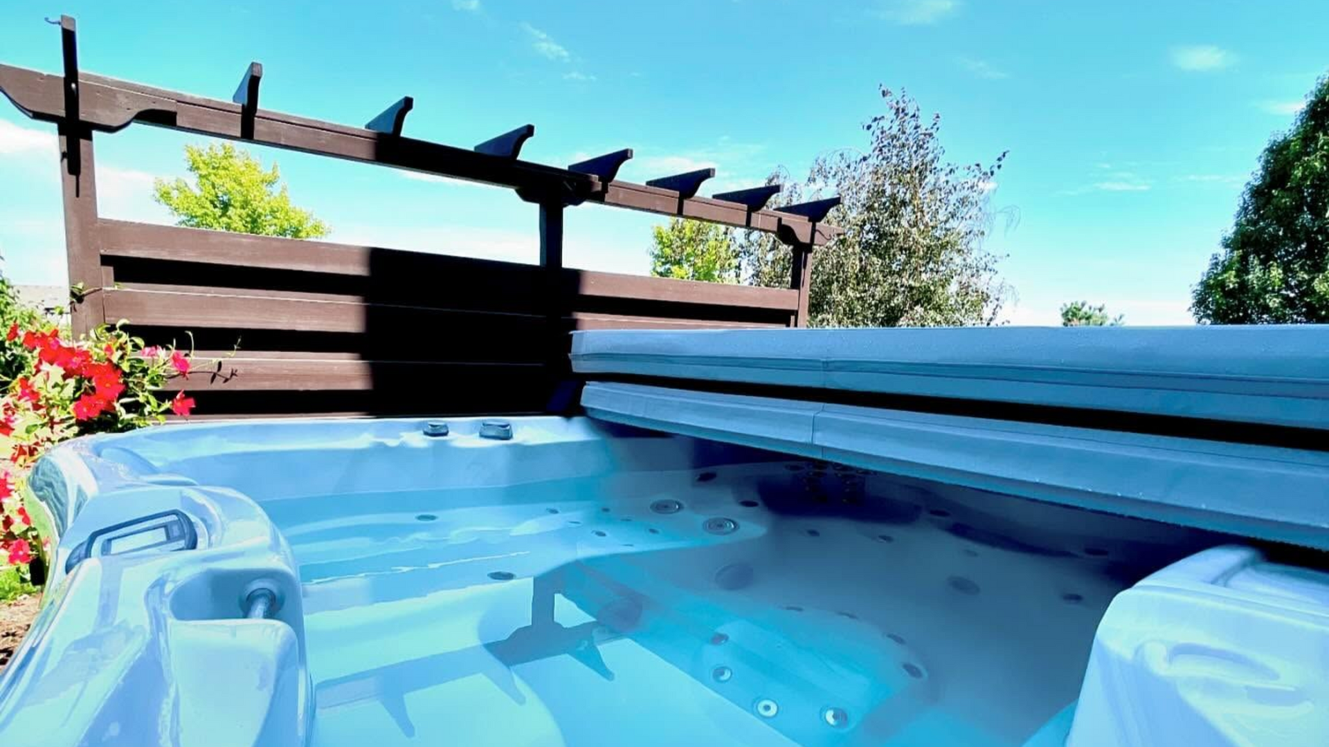 Hot tub filled with blue water, under a wooden pergola on a sunny day.