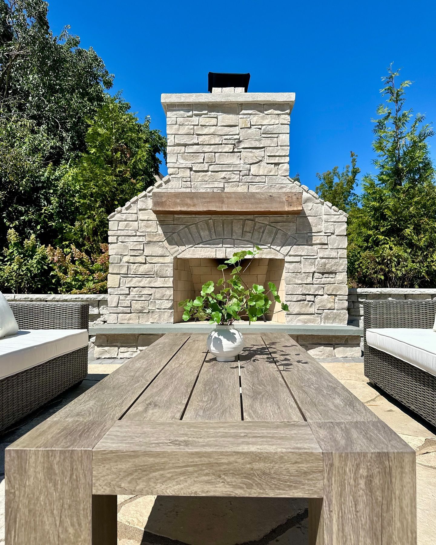Outdoor stone fireplace with wooden table and seating on a sunny day.