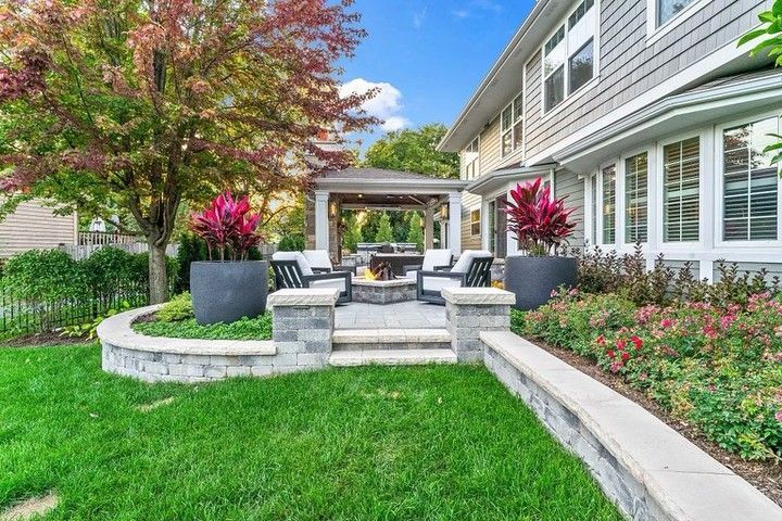 Backyard patio with fire pit, seating, and a gazebo near a two-story gray house.