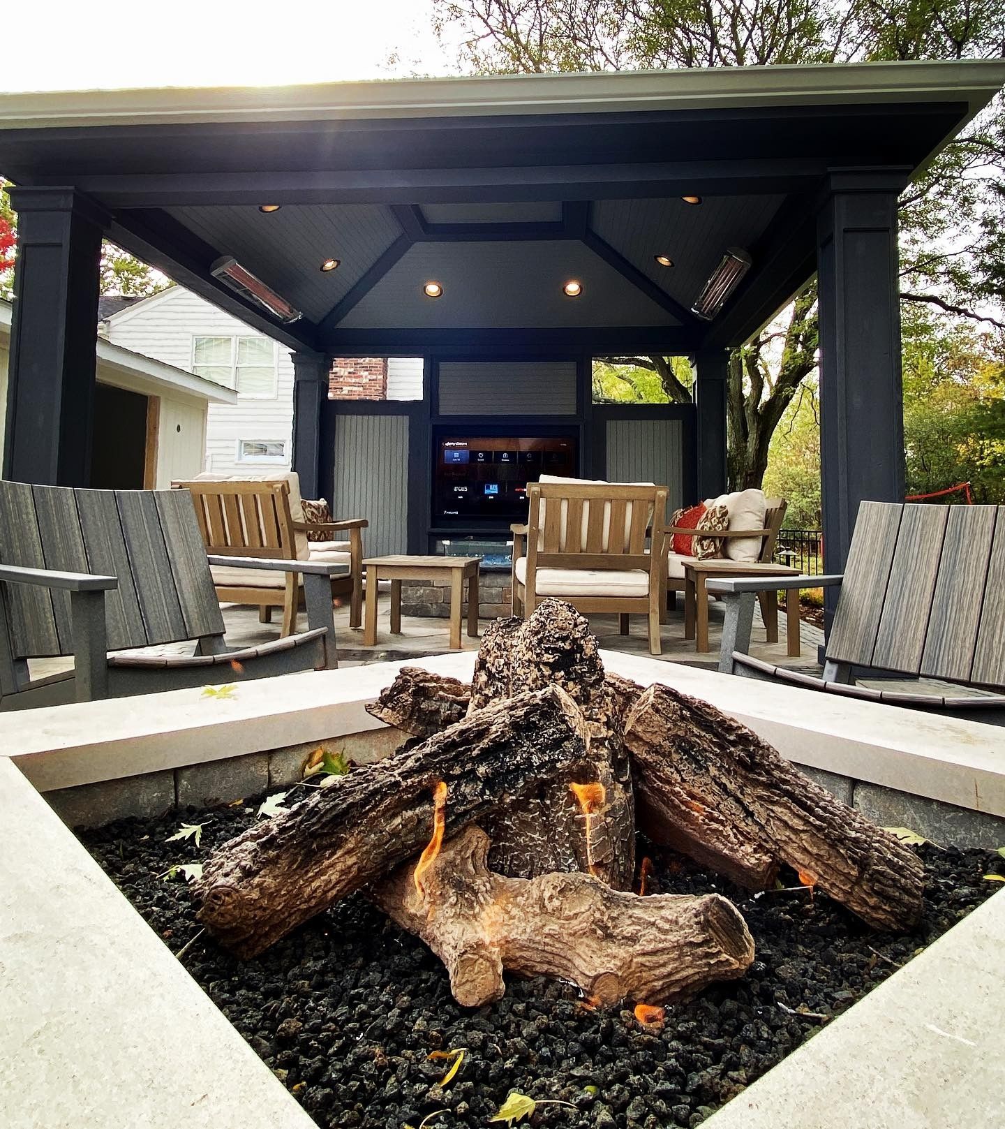 Outdoor living area with fire pit and seating under a covered structure with a TV.