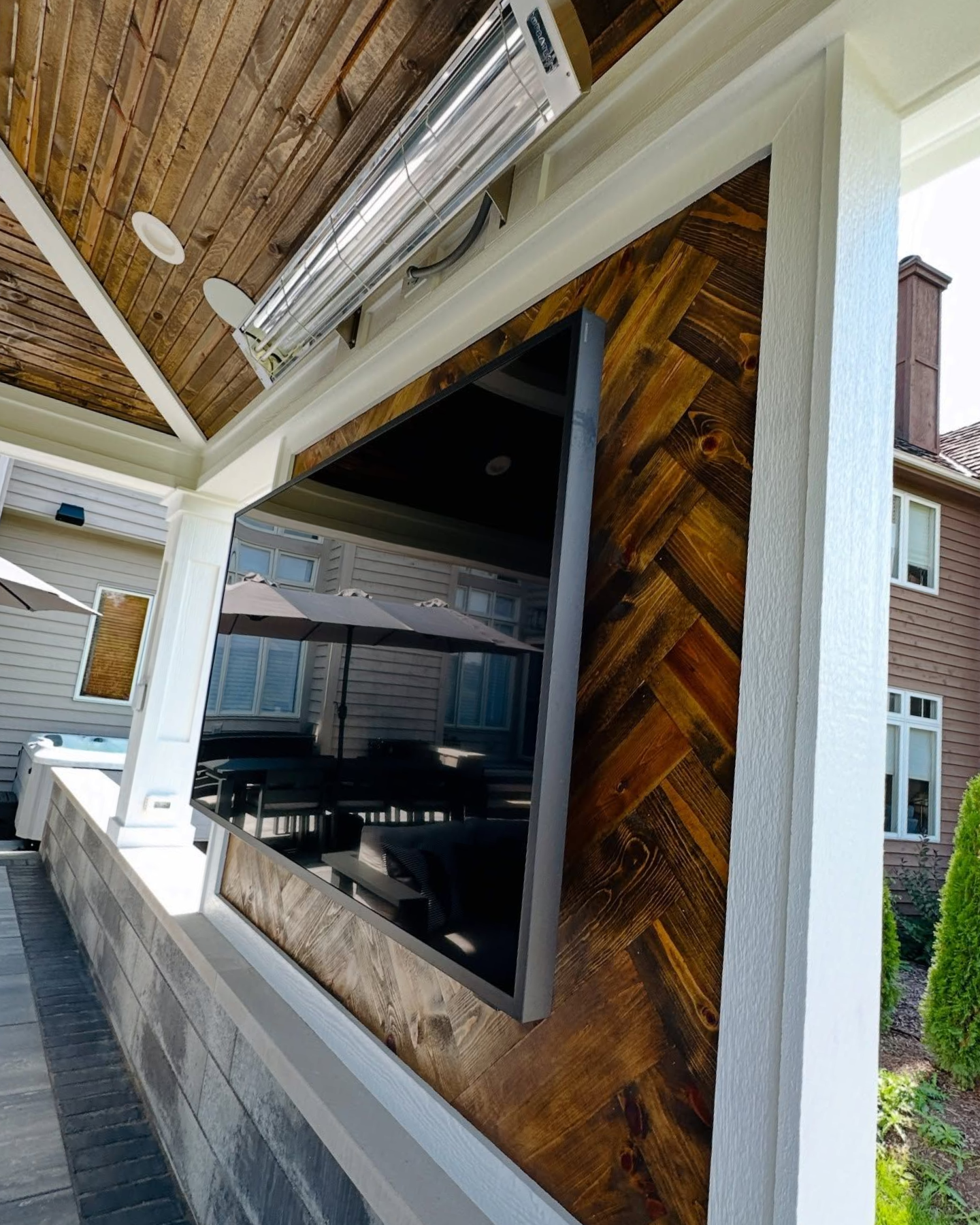 Outdoor entertainment area with herringbone wood accent around large TV.
