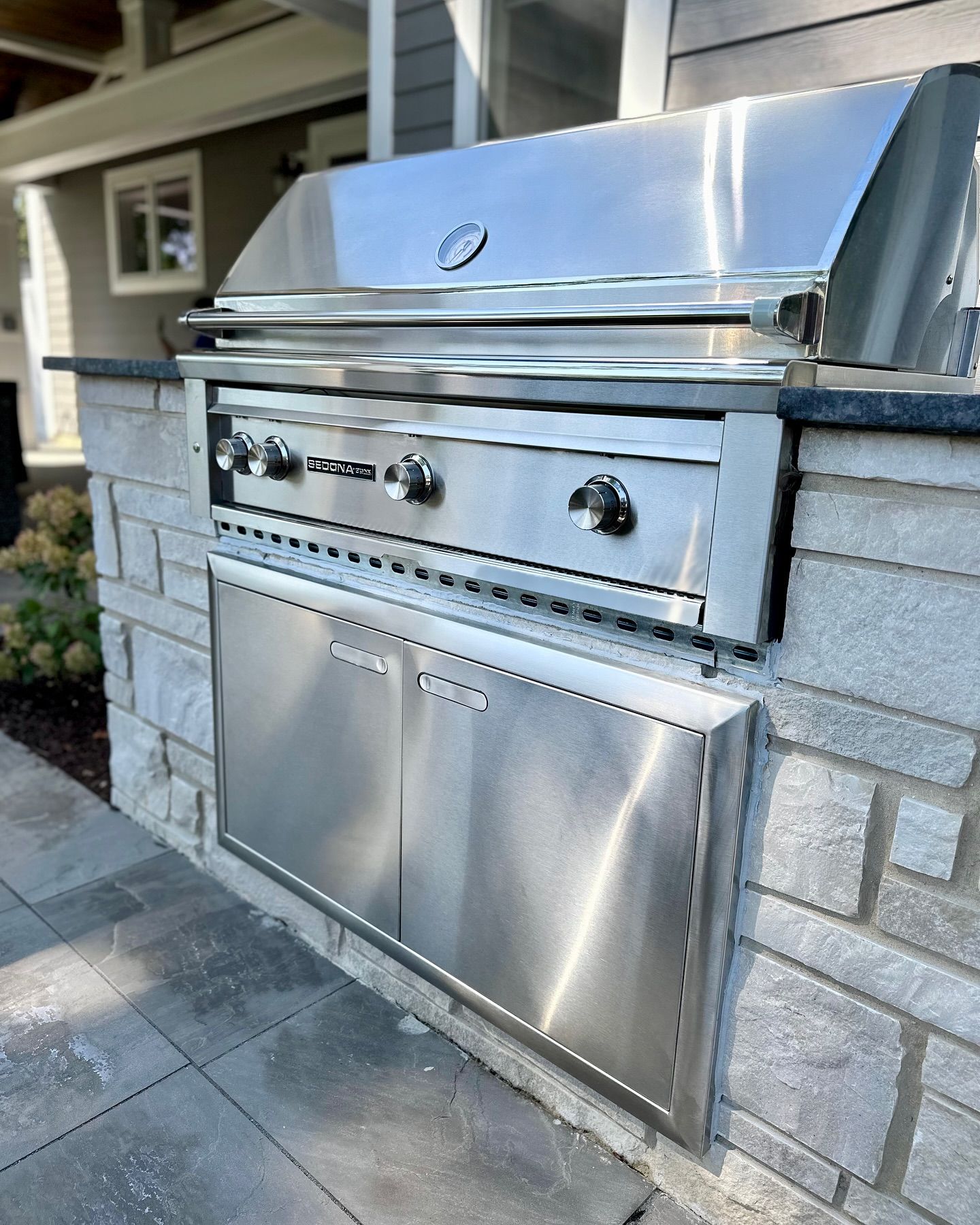 Stainless steel outdoor grill built into a stone wall with a storage cabinet.