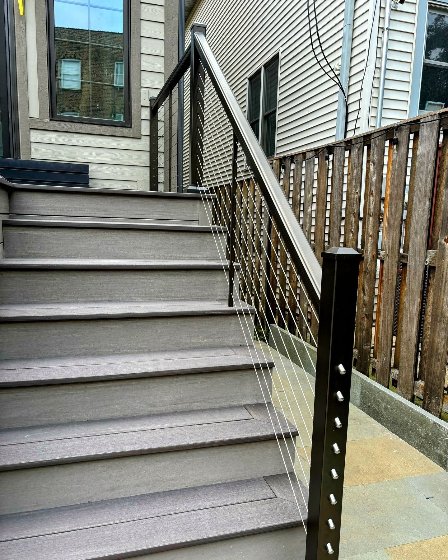 Wooden stairs with gray treads and cable railing, leading to a doorway.