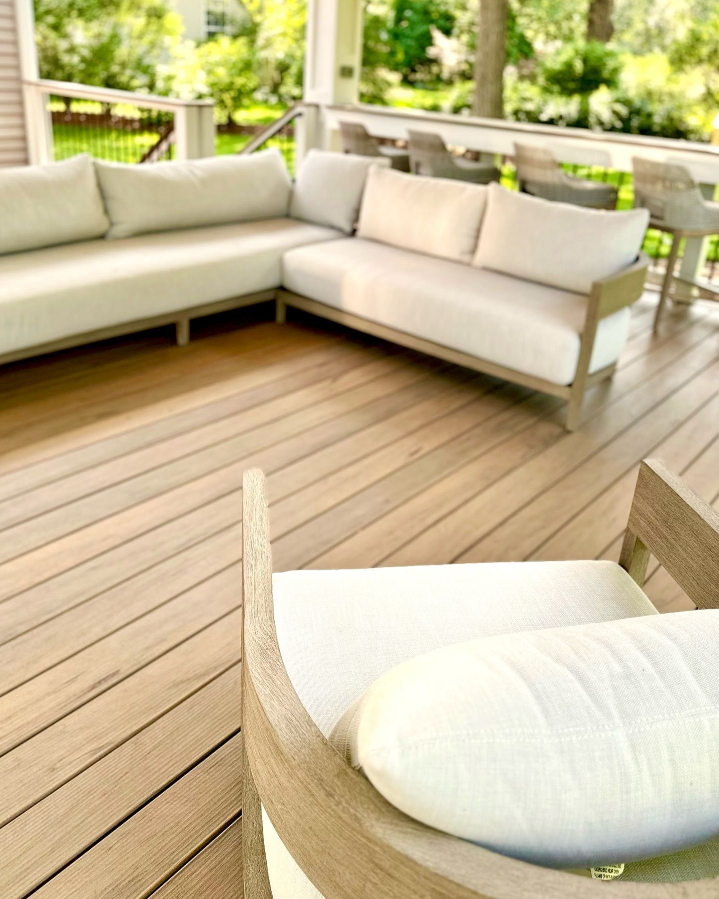 Outdoor deck with sectional sofa and armchair. Beige cushions, light wood deck and frame.
