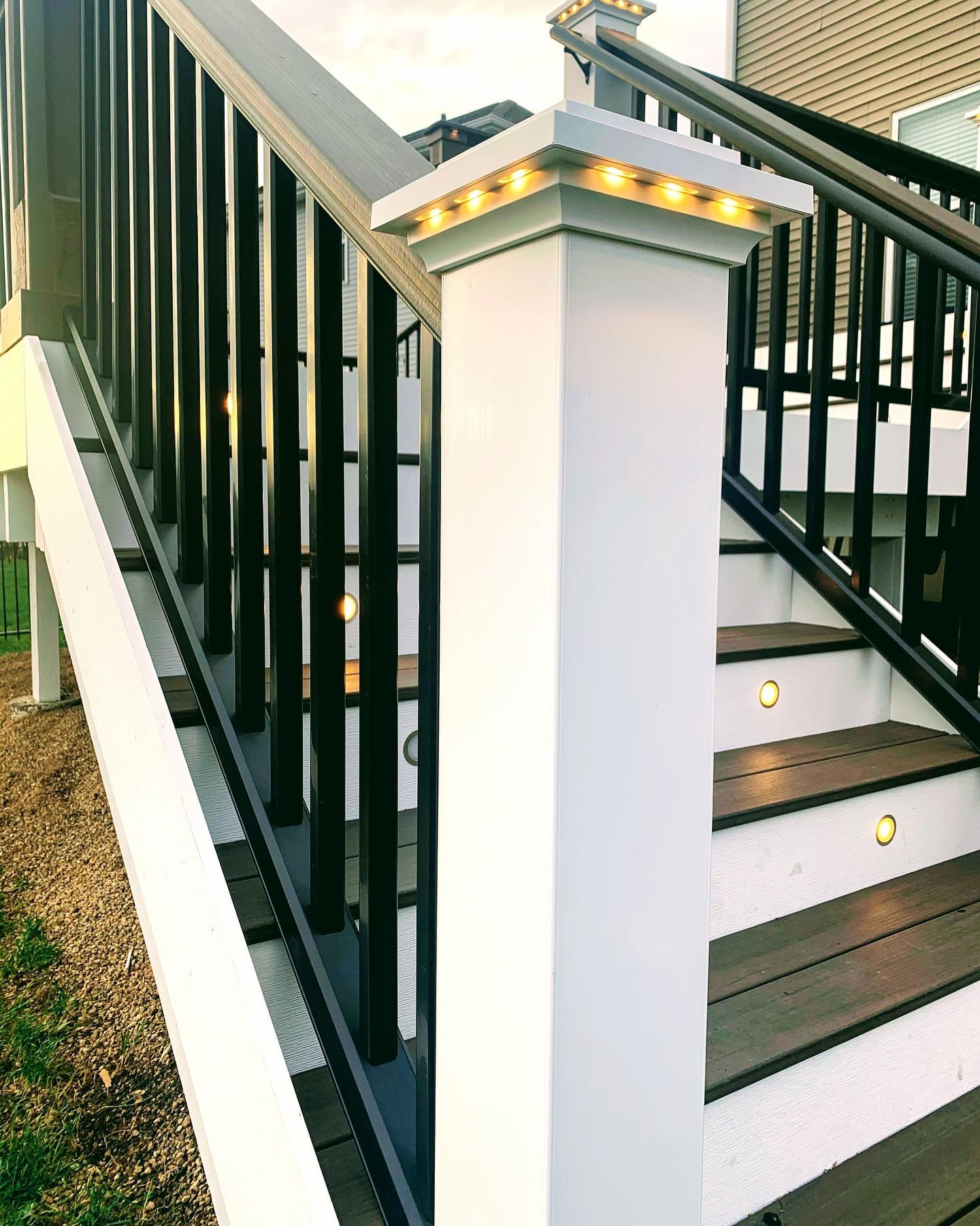 White and black deck stairs with built-in lights. Top of a post has small yellow lights.
