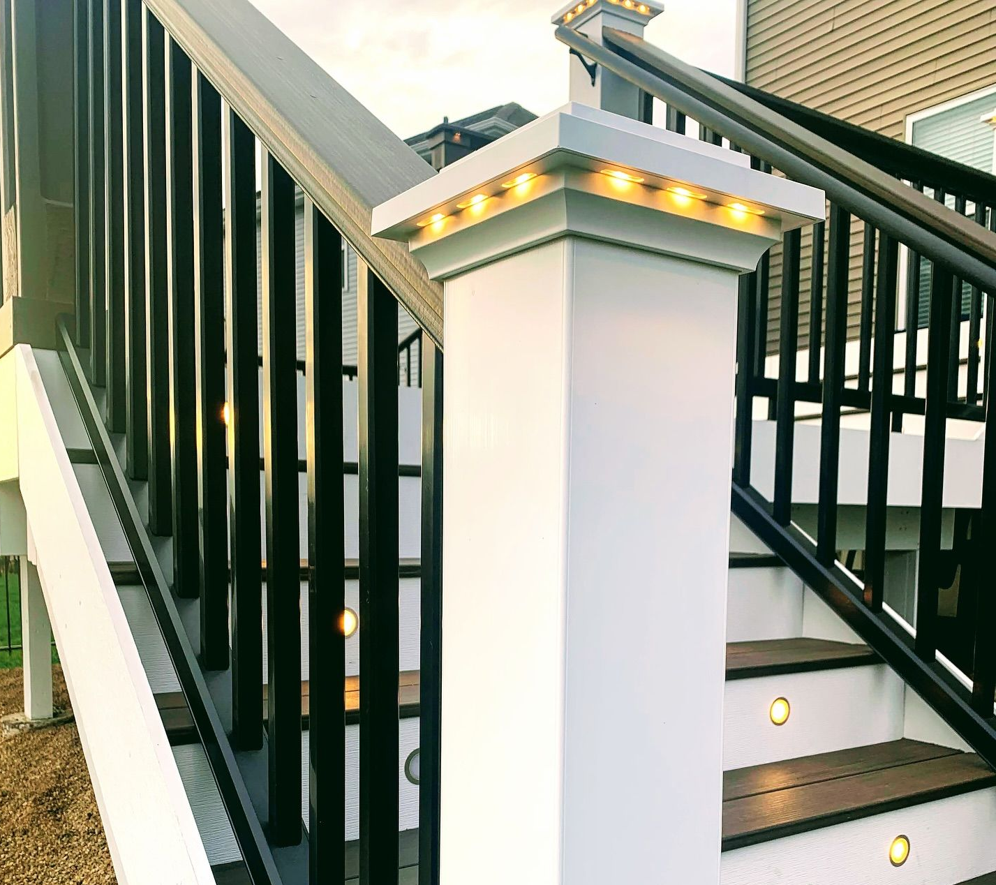 White deck posts with integrated lights, black railings, and steps.