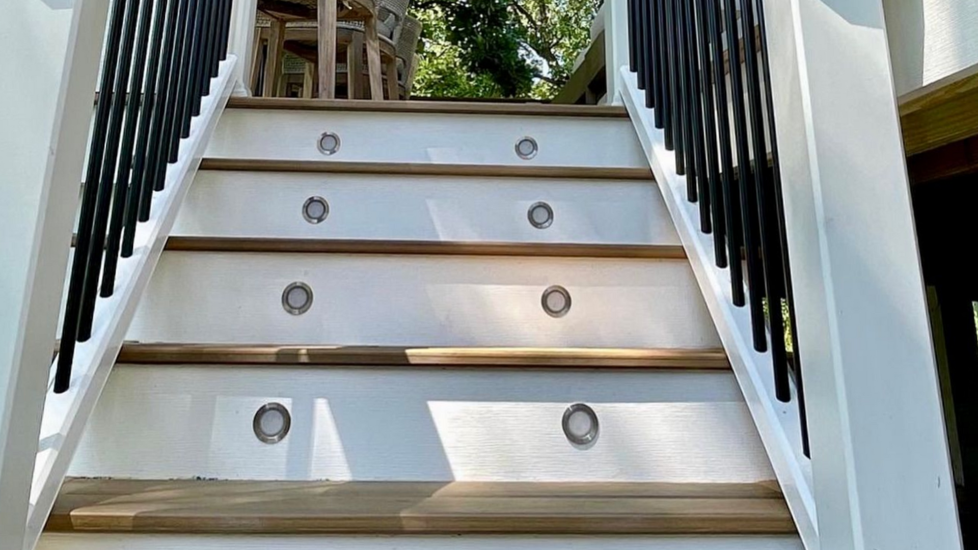 Wooden outdoor stairs with white risers, brown treads, black railings, and embedded lights.