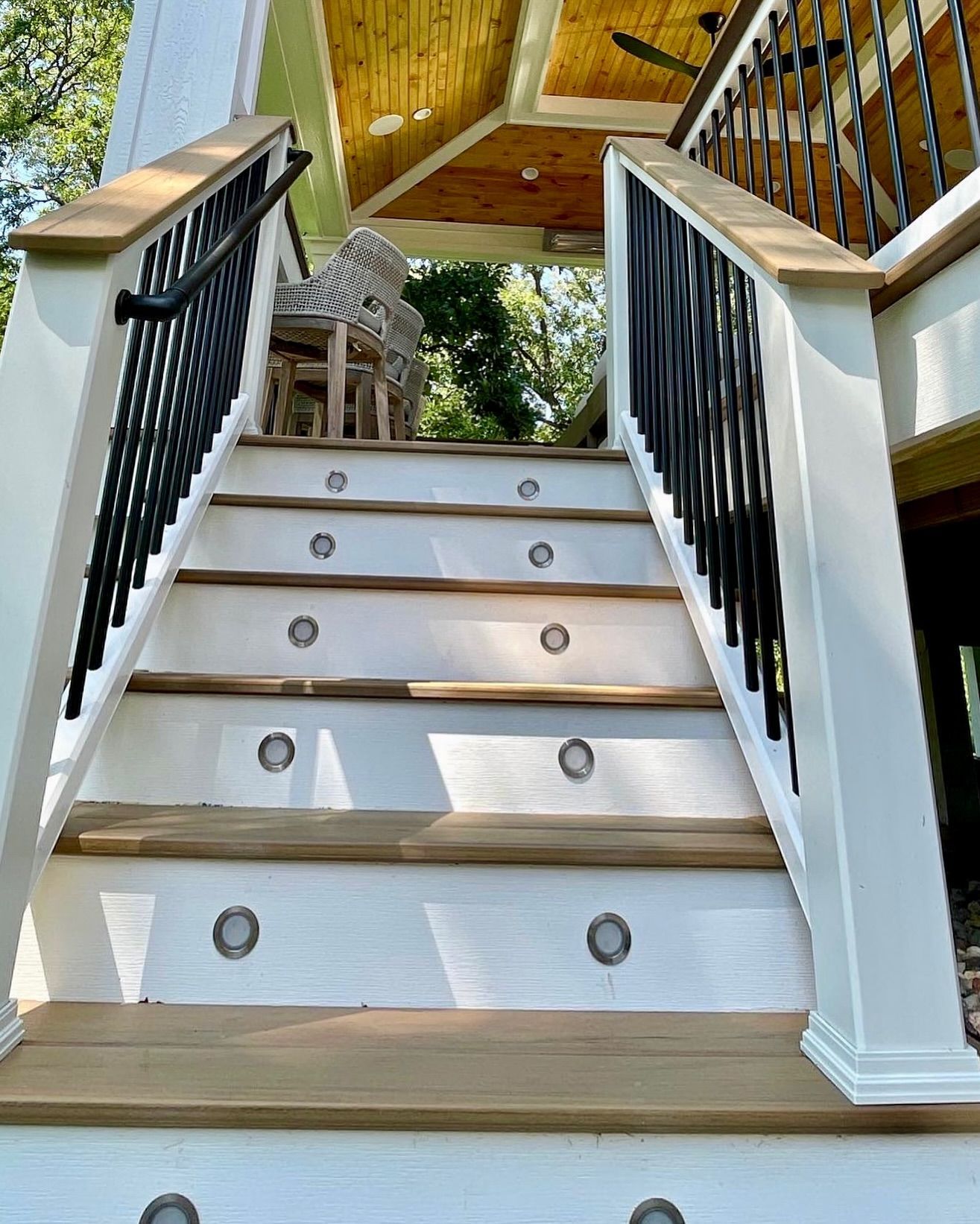 Staircase leading up with white risers, wooden treads, black railing, and built-in lights.