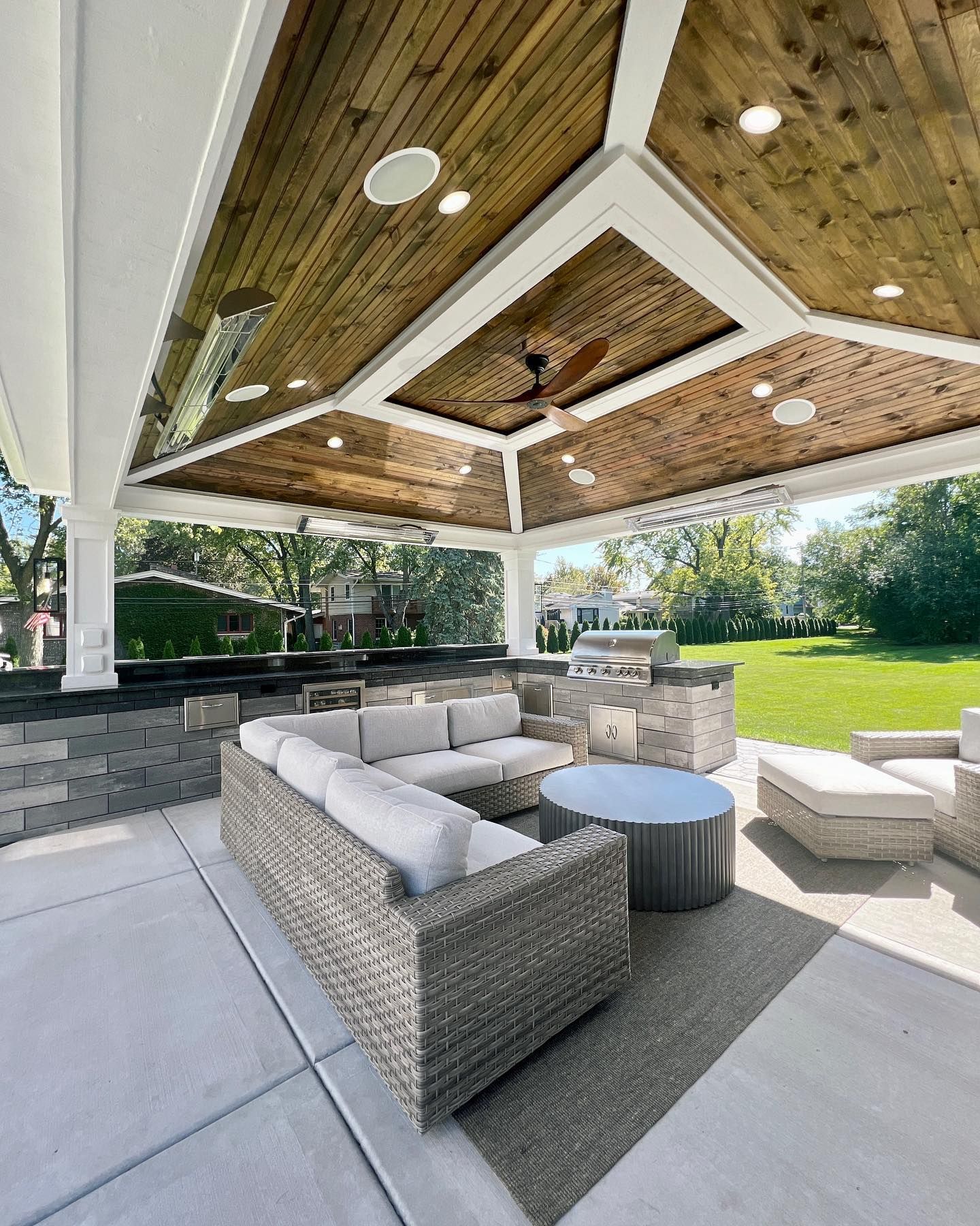 Outdoor covered patio with gray furniture, built-in grill, and wood ceiling.