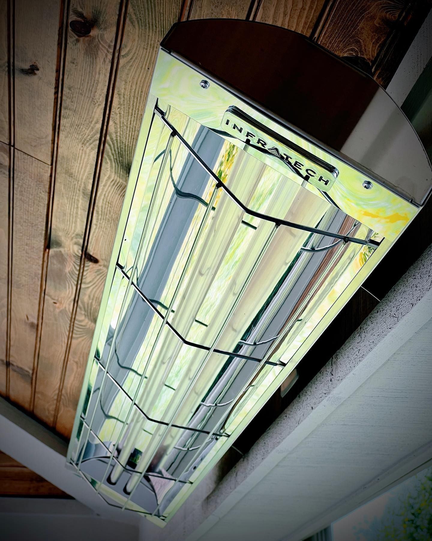 Ceiling-mounted infrared heater, light yellow, with protective cage, mounted on wooden ceiling.