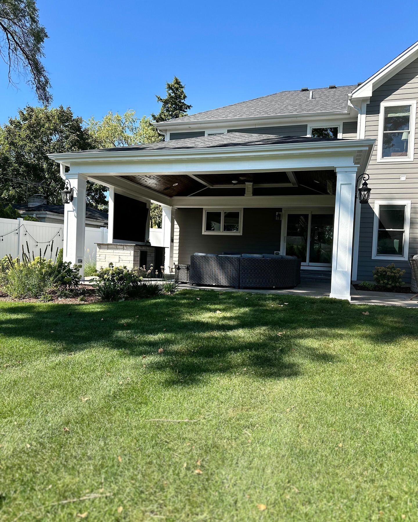 Backyard with covered patio, hot tub, and house; green grass and clear sky.