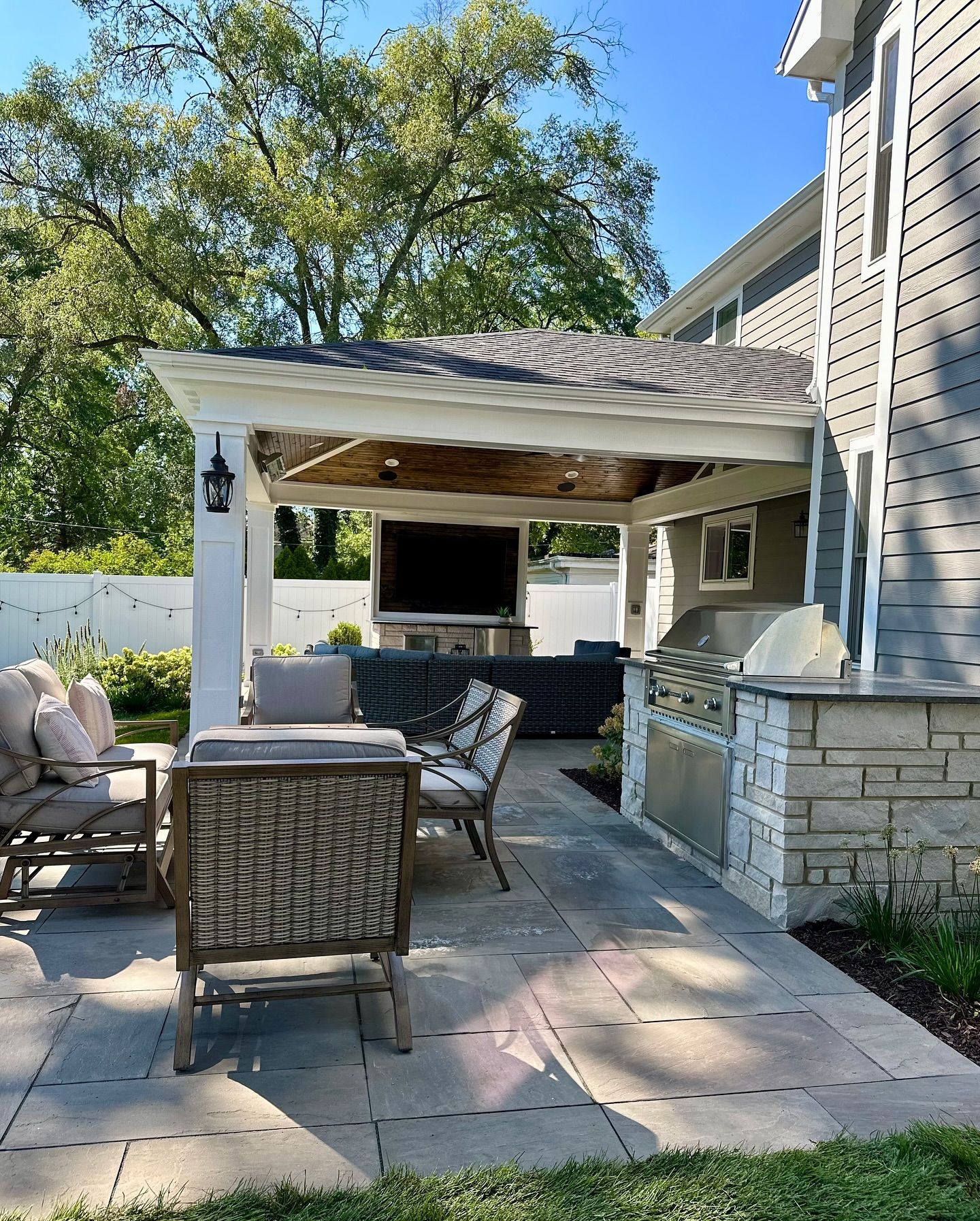 Outdoor patio with pergola, seating area, built-in grill, and large TV.