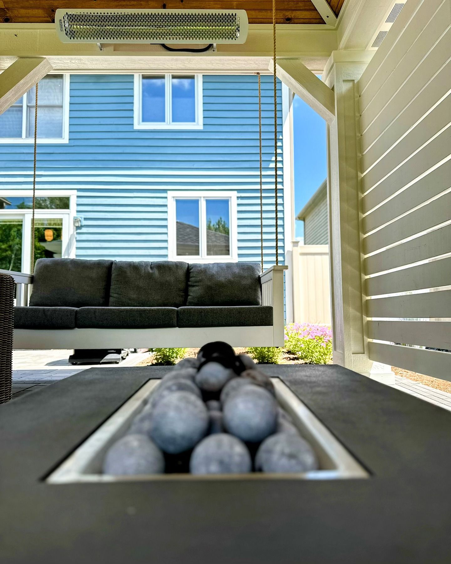 Outdoor patio with a swing, fire pit, and blue house in the background.