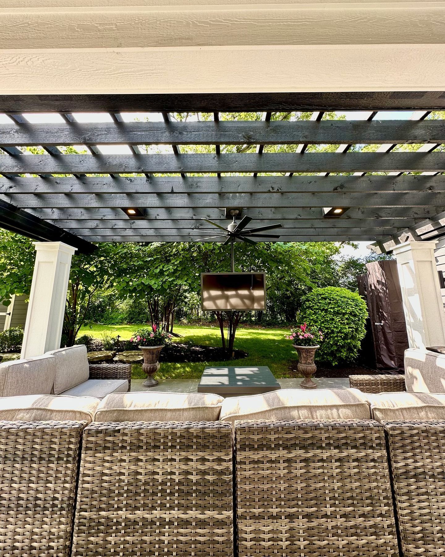 Outdoor patio with wicker furniture, a pergola, and a view of a garden.