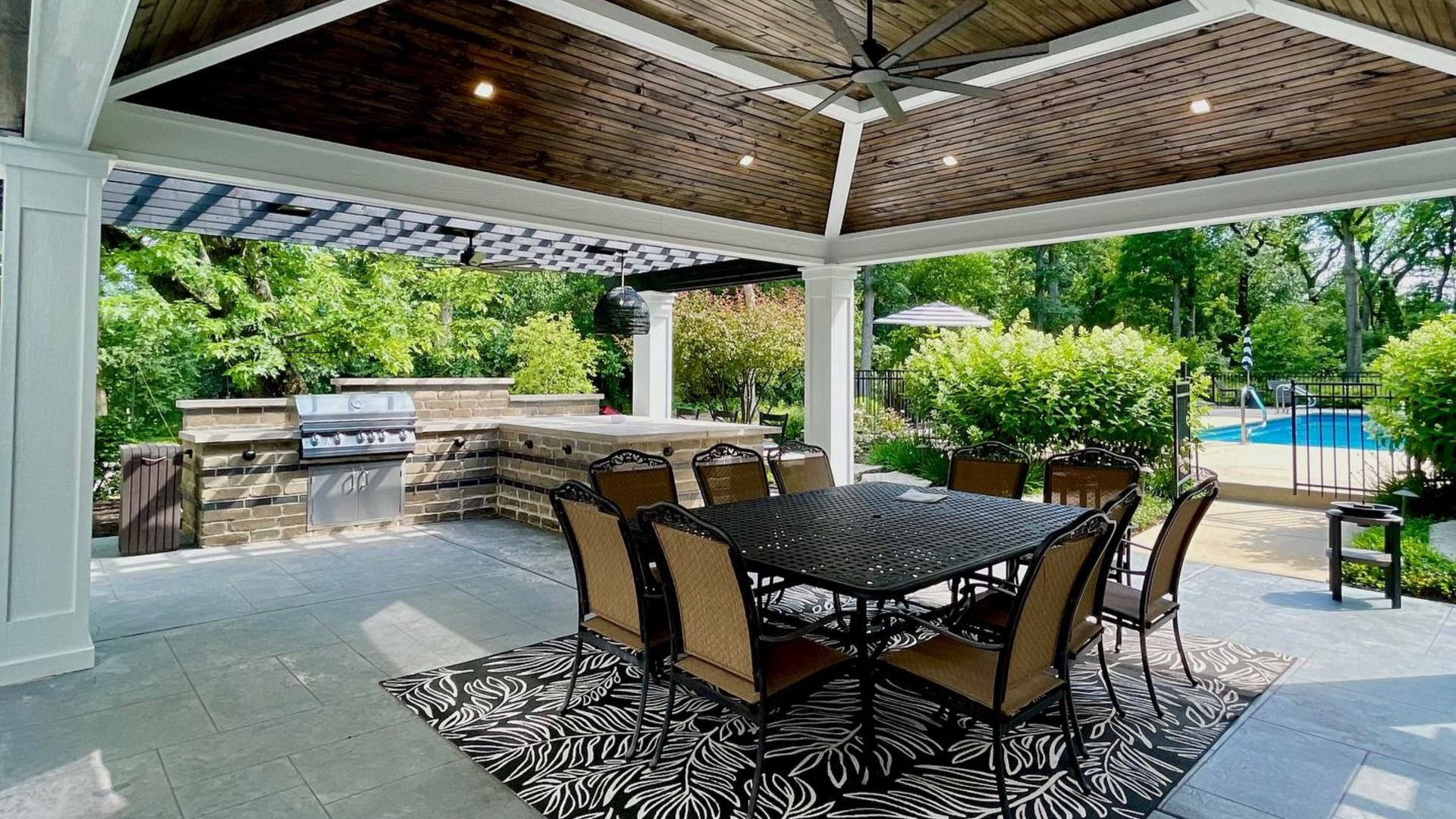 Patio with dining table, outdoor kitchen, and swimming pool visible in the background.