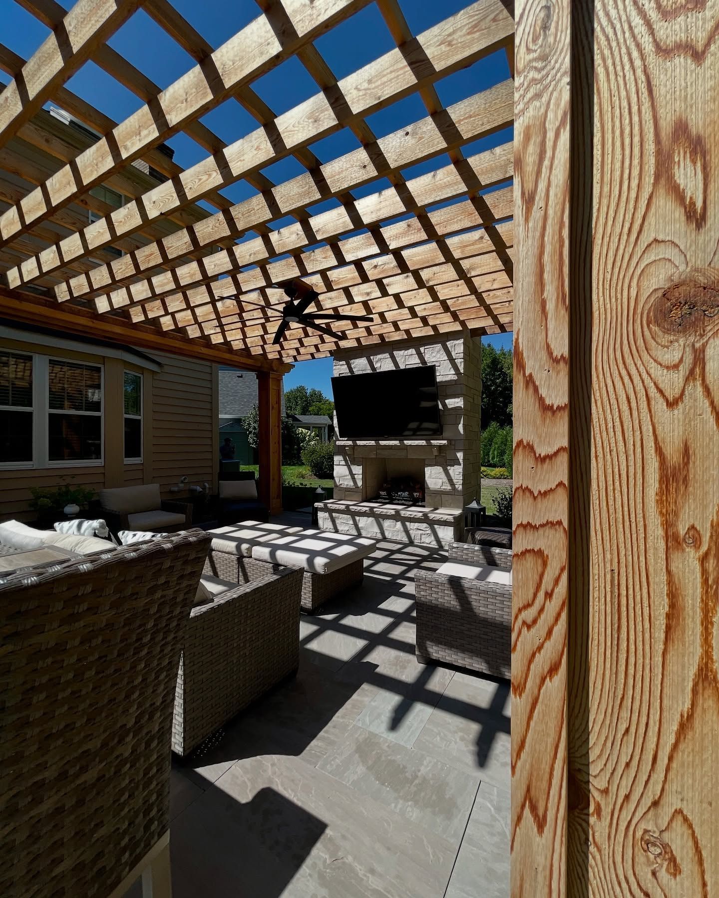 Wooden pergola over outdoor seating area with a TV and fireplace.