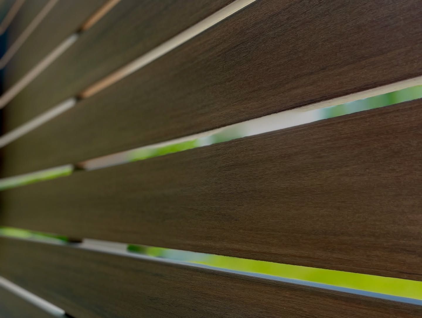 Wooden slat fence with blurred green background.